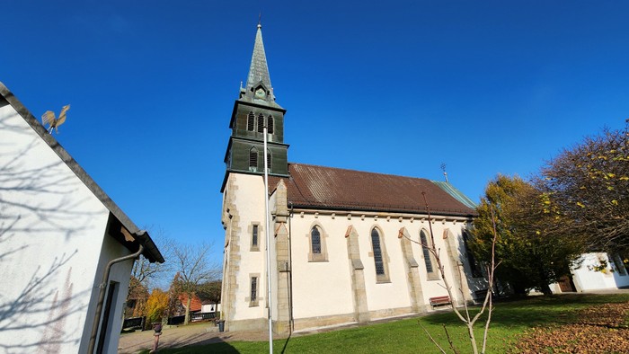 Kirchengebäude mit hohem Turm und spitzem Dach vor blauem Himmel
