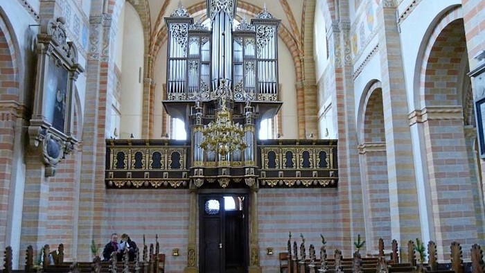 Elegant kirkeinteriør med prægtigt pibeorgel og træbænke under hvælvede murstensvægge og et detaljeret loft.