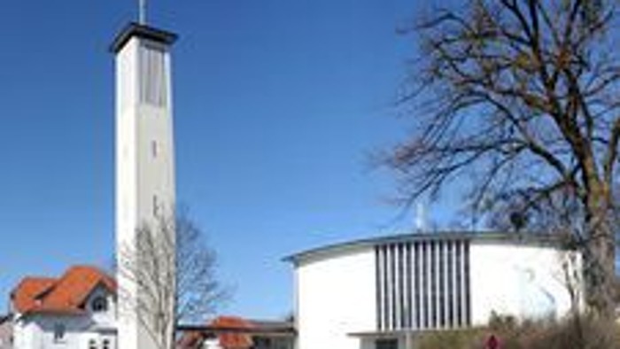 Moderne Kirche mit hohem Glockenturm und runder Kapelle in einer ruhigen, landschaftlich gestalteten Umgebung.