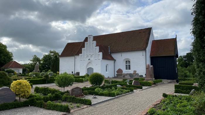 Et hvidt historisk hus med røde tag og en have med stenveje og planter.