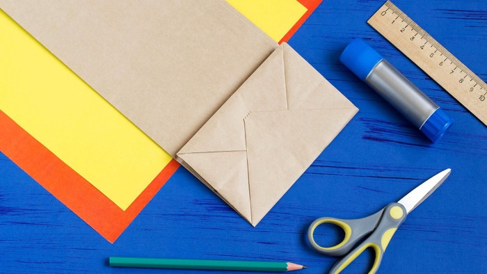 Neben farbigem Papier liegen Bleistift, Schere, Kleber und Lineal.