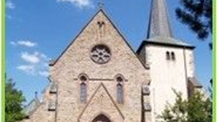 Historische Steinkirche mit Uhrturm und spitzen Türmen vor einem strahlend blauen Himmel.