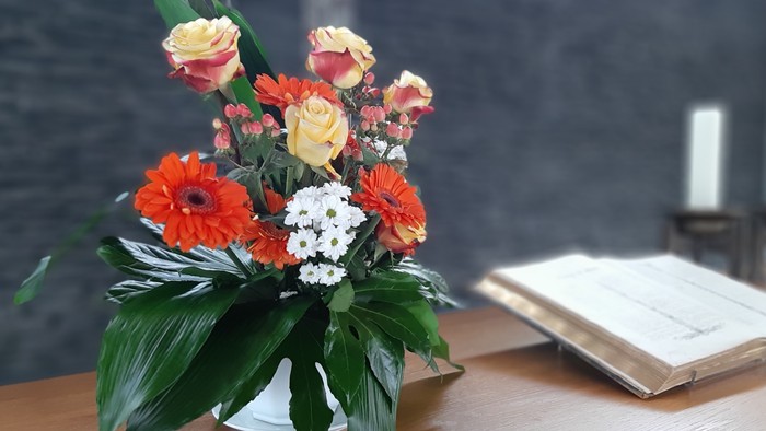 Ein Blumenstrauß mit roten und gelben Blumen steht auf einem Holztisch neben einem aufgeschlagenen Buch.