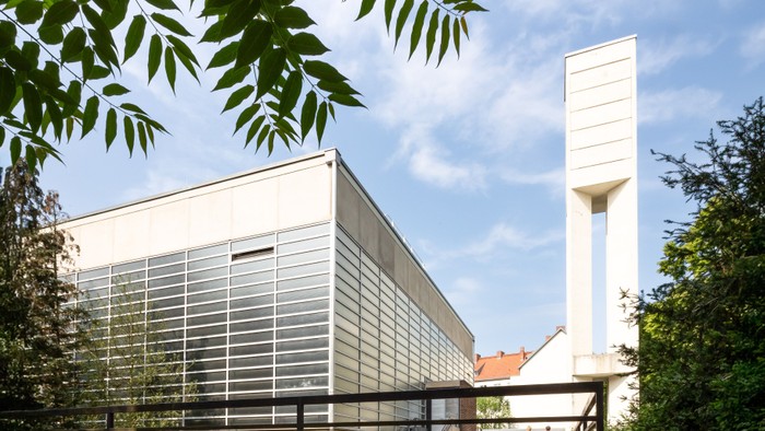 Moderne Kirche mit hohem Turm und Glasfassade, umgeben von Bäumen
