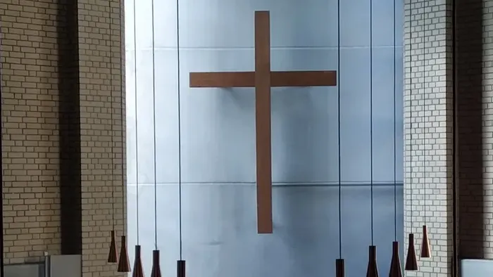 Ein Kircheninneres mit einem großen Holzkreuz an der Wand und mehreren Hängelampen.