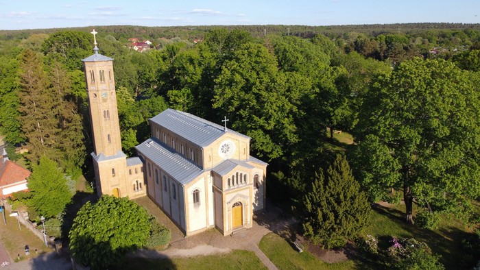 Luftaufnahme einer idyllischen Kirche, umgeben von üppigem Grün und hohen Bäumen.