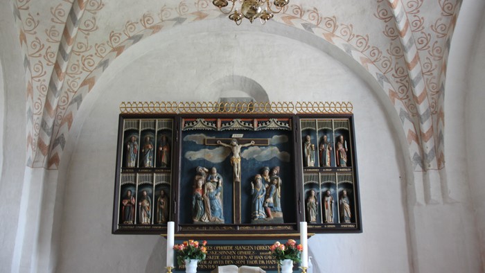 Alter Nr. Løgum kirke, hvorover der ses loftets buer med et kalkmaleri-mønster malet på i sarte farver.