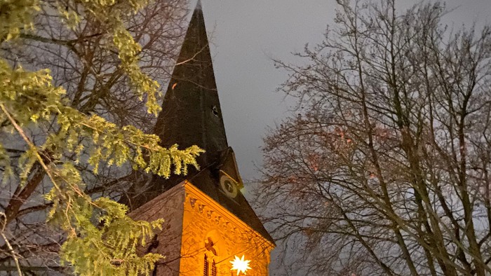 Ein historischer Kirchturm, beleuchtet in der Abenddämmerung, gerahmt von kahlen Winterbäumen.