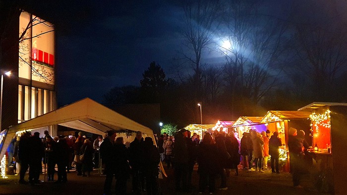 Vor der Immanuel-Kirche tummeln sich viele Besucher bei Vollmond vor hell erleuchteten Adventsbuden