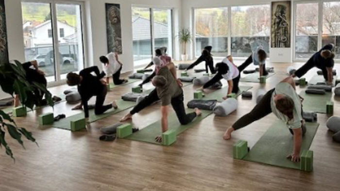 Eine Yoga-Stunde im Gange, bei der Teilnehmer:innen in einem hellen, geräumigen Studio Plank-Positionen auf ihren Matten ausführen.