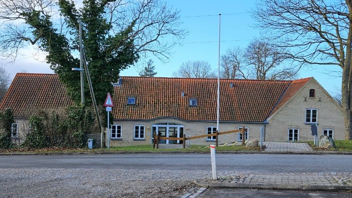 En hvid bygning med rødt tag og træer foran