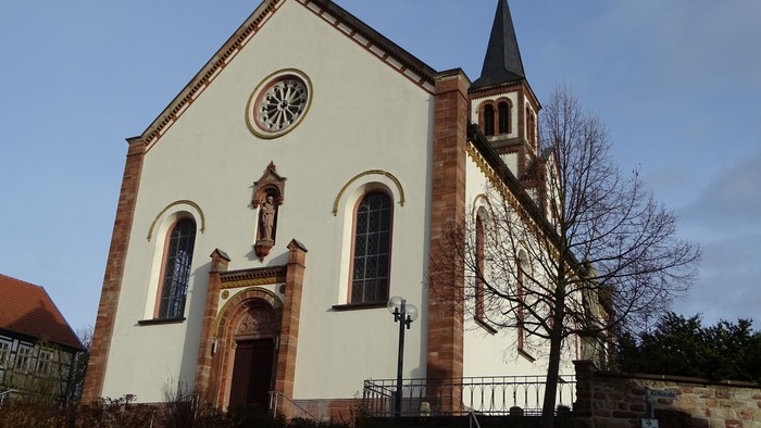 Kirchengebäude mit Uhr und Kreuzigungsgruppe vor weißem Fassadenanstrich