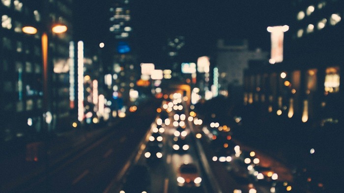 Belebte Stadtstraße bei Nacht mit unzähligen Lichtern und hohen Gebäuden.