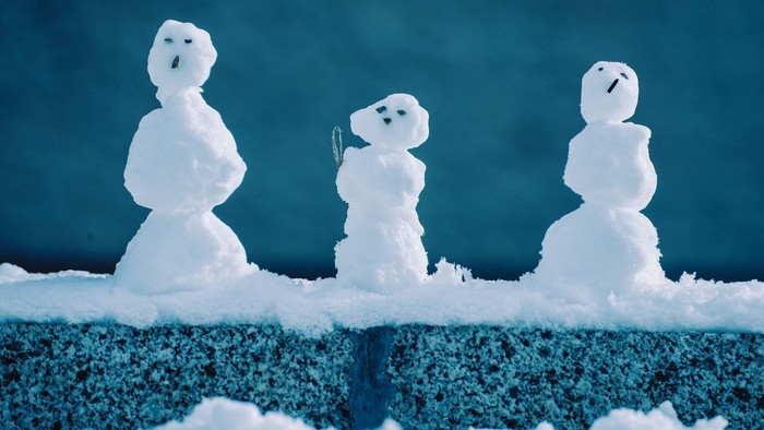 Tre små snepeople står i rad i sneen.