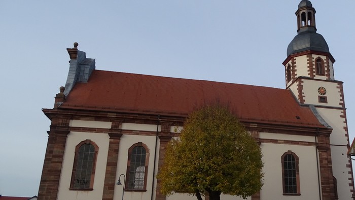 Kirchengebäude mit rotem Dach und hohem Turm neben Baum