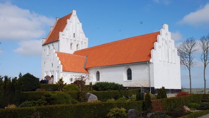 Et hvidt kirkebygning med røde tag og omgivelser med grønne planter og sten.