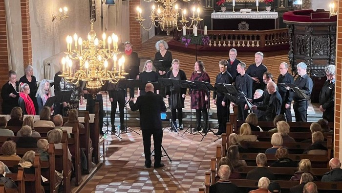 Et kor optræder i en kirke med et opmærksomt publikum siddende på træbænke.