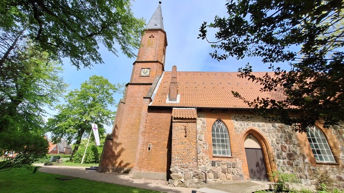 Kirchengebäude aus rotem Backstein mit Uhrturm und grünem Rasen