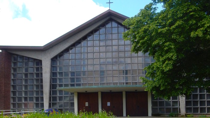 Moderne Kirche mit Glasfassade und Kreuz auf dem Dach, umgeben von blühendem Gras und Bäumen