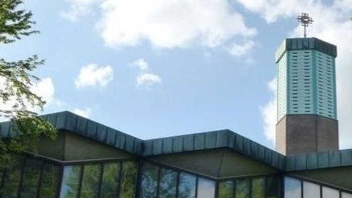 Ein modernes Gebäude mit Glasfront und einem markanten Kamin unter blauem Himmel