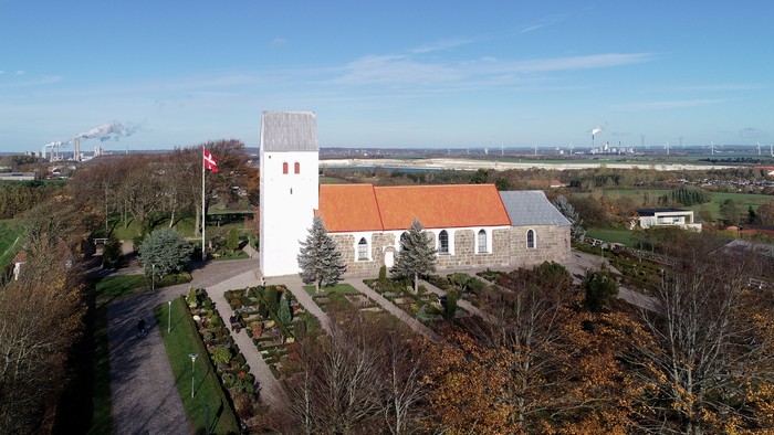 En lille kirke med klokketårn og rødt tag i landlig omgivelse