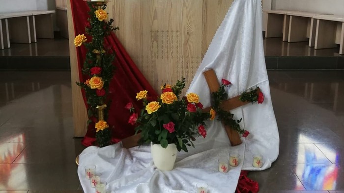 Osteraltar mit Kerzen, Blumenschmuck und einem verhüllten Holzkreuz in einer Kirchenumgebung.