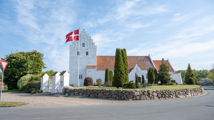 En hvid kærmisk tårn med rødt tag og dansk flag på en stenmur ved en vej
