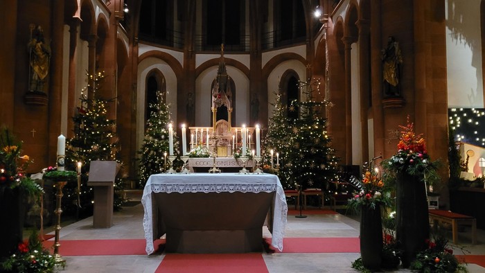 Kircheninneres, weihnachtlich geschmückt mit Bäumen, Kerzen und religiösen Symbolen.