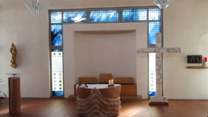 Ein runder Altar mit zwei brennenden Kerzen vor einem großen Kreuz aus Marmor.
