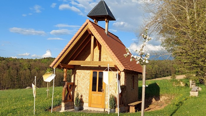 Idyllische Holzkapelle mit Glockenturm, eingebettet in eine üppige, grüne Landschaft.