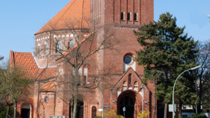 Große rote Backsteinkirche mit hohem Turm und spitzem Dach.