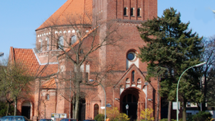 Große rote Backsteinkirche mit hohem Turm und spitzem Dach.