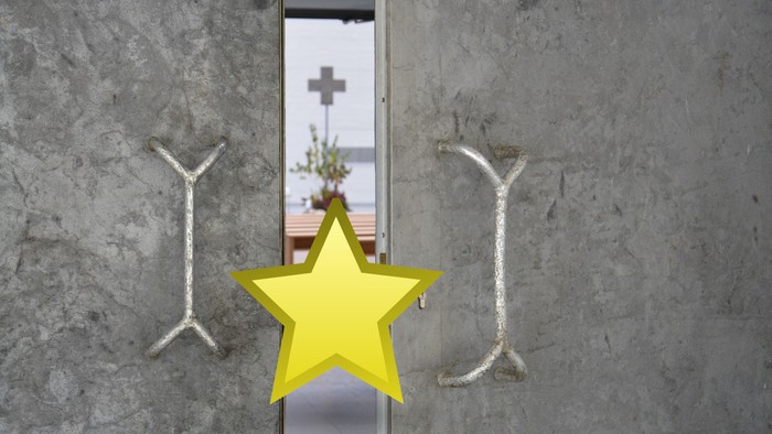 Zwei silberne Hakenkreuze flankieren eine gelbe Sternikone an einer Betonwand