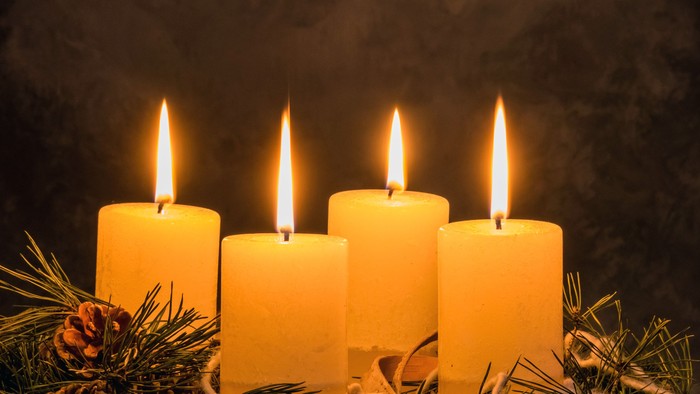 Vier brennende Kerzen auf dunklem Hintergrund mit Tannenzweigen