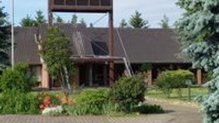 Das Bild zeigt ein Holzhaus mit Schindeldach in einem Garten.