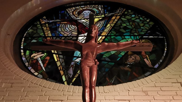 Eine Kreuzigungsstatue vor einem bunt gefärbten Glasfenster in einer Kirche