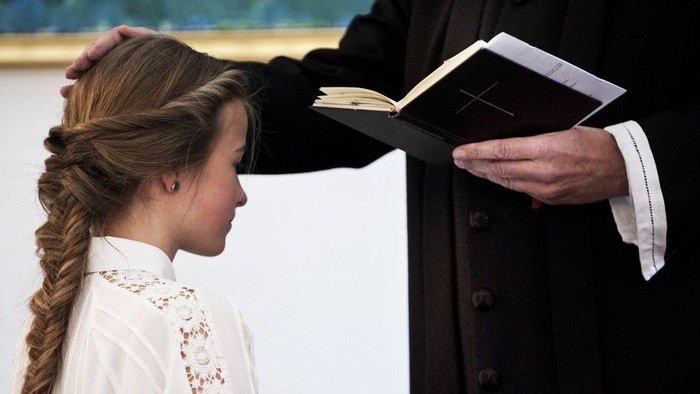 En kvinde med frisyr ser på en bog, som en mand i mørkt tøj holder op for hende