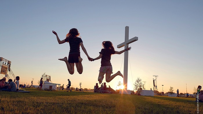 Zwei Mädchen springen vor Kreuz bei Sonnenuntergang