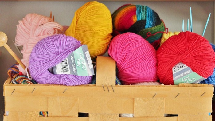 Farverige garnnøgler pænt arrangeret i en træopbevaringskasse med strikkepinde.