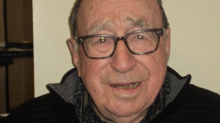 An elderly man wearing glasses and a striped shirt.