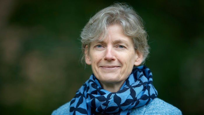 En kvinde med kort hår og blå skjorte med mønster.