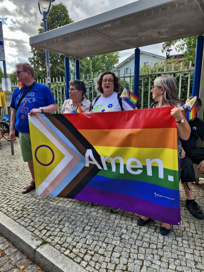 Vertreter*innen der Kirche mit einem Regenbogen-Banner auf dem Amen steht