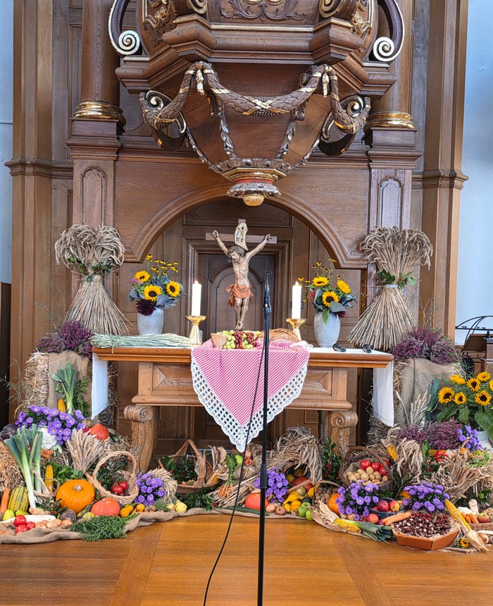Blumen, Früchte, Getreideähren, Gemüse und Obst schmücken einen Altar auf dem ein Kruzifix steht und zwei erleuchtete Kerzen.