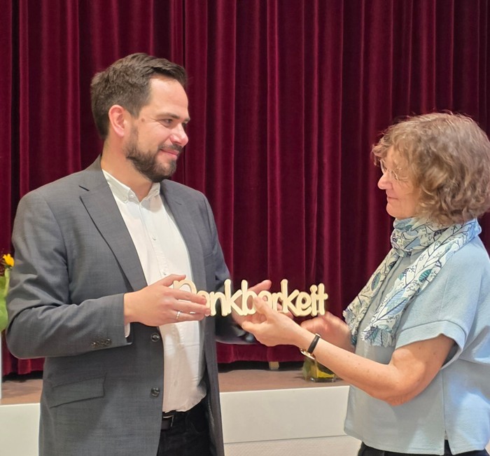 Ein Mann übergibt einer Frau einen hölzernen Schriftzug Dankbarkeit.