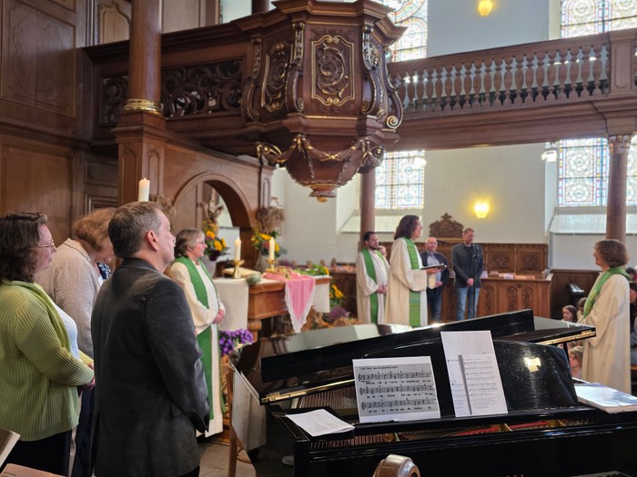 Hinter einem Klavier stehen Menschen vor einem Altar, um eine Pfarrerin zu verabschieden.
