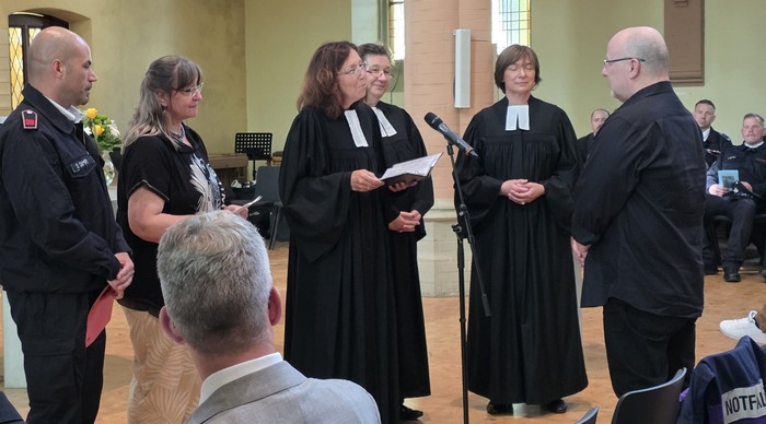 Pfarrer Uli Geiler steht vor Menschen, die ihn in einem Kirchenraum ansprechen. 