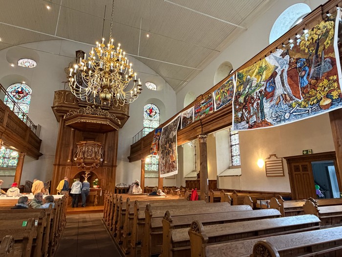 Bunte Tücher hängen von den Emporen einer Kirche im Kirchenraum schauen sich Besucherinnen um.