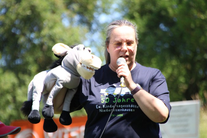 Gemeinsam mit ihrer Handpuppe Joni begrüßt Pfarrerin Hilke Perlt die Gäste des Kindergartenjubiläums und erklärt auf kindgerechte Weise, warum dieser Tag überhaupt gefeiert wird. (Foto: Sascha Valentin)