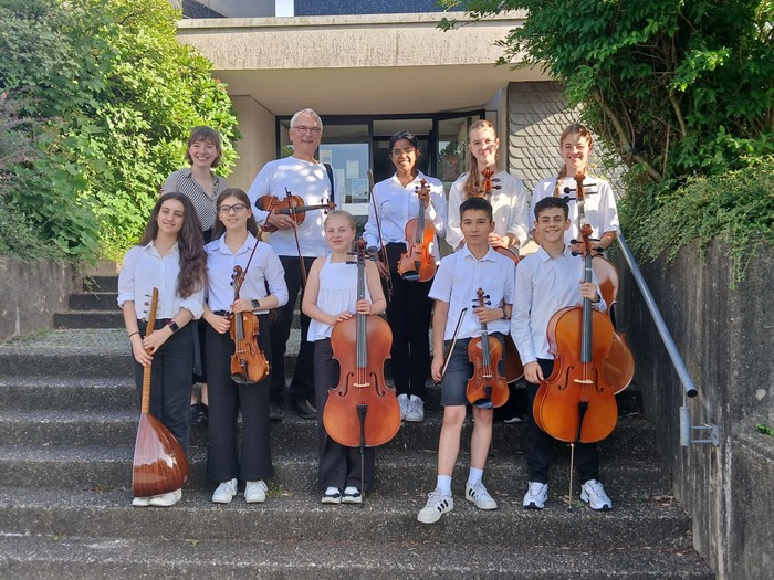 Eine Gruppe junger Musiker in einheitlichen Hemden posiert mit verschiedenen Streichinstrumenten auf einer Freitreppe.