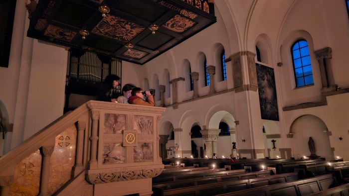 Bei der Berliner Familiennacht in St. Marien Liebfrauen schauen Kinder von der Kanzel herab auf den mit Kerzen beleuchteten Kirchenraum.